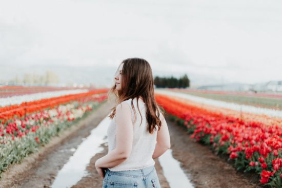 woman in white top looks over flower fields with hands in pockets